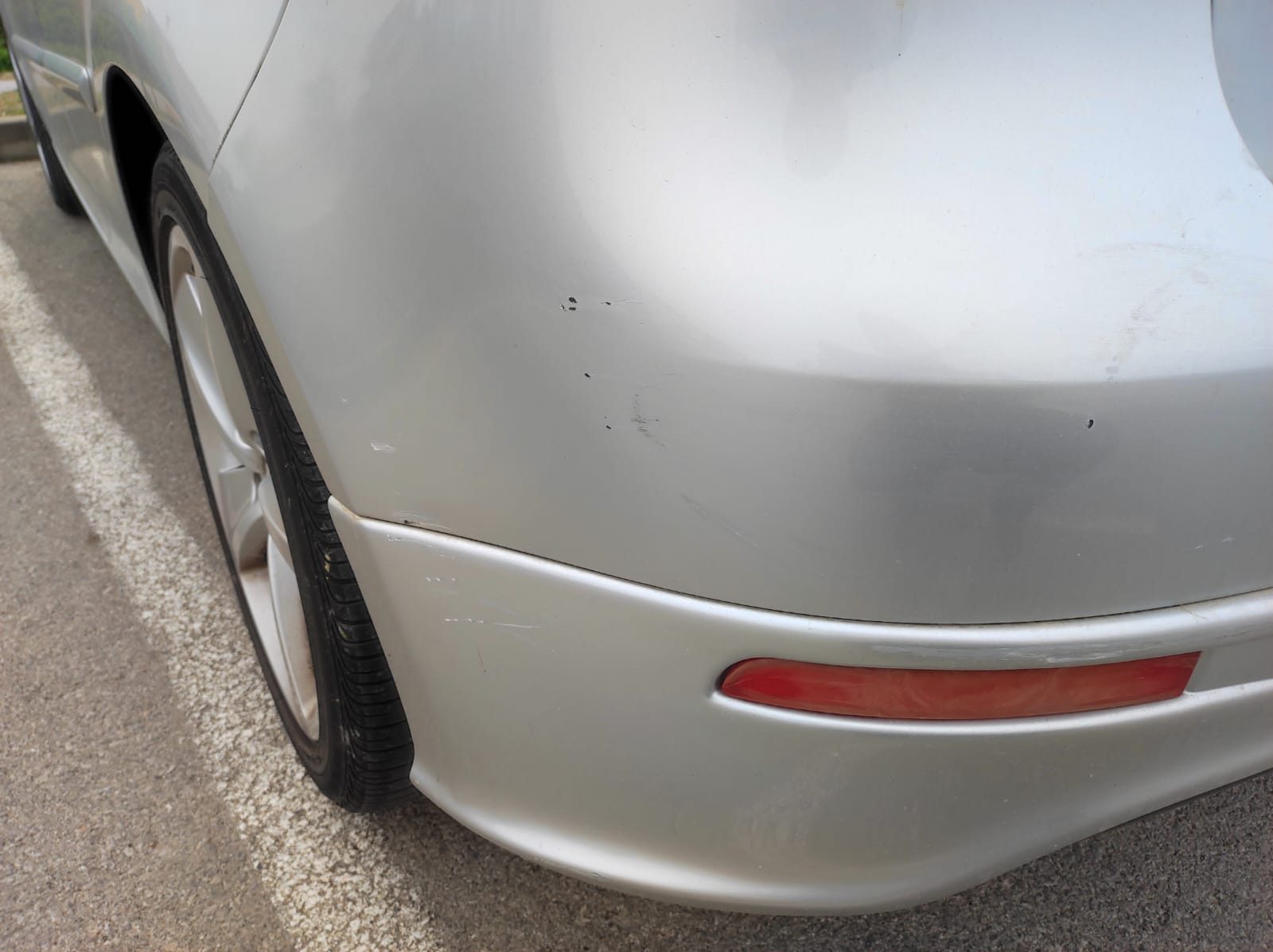 Detalj stražnjeg branika srebrnog automobila s tragovima oštećenja